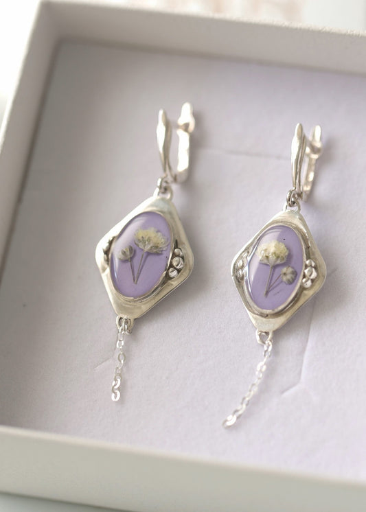 A pair of silver earrings with purple floral designs, displayed in a box.