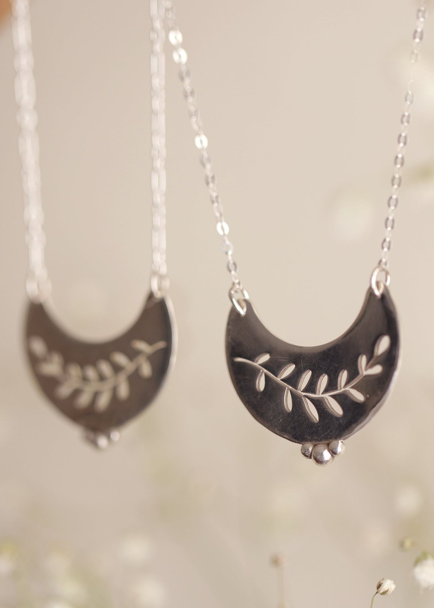 Silver crescent moon necklaces with leaf designs on a neutral background
