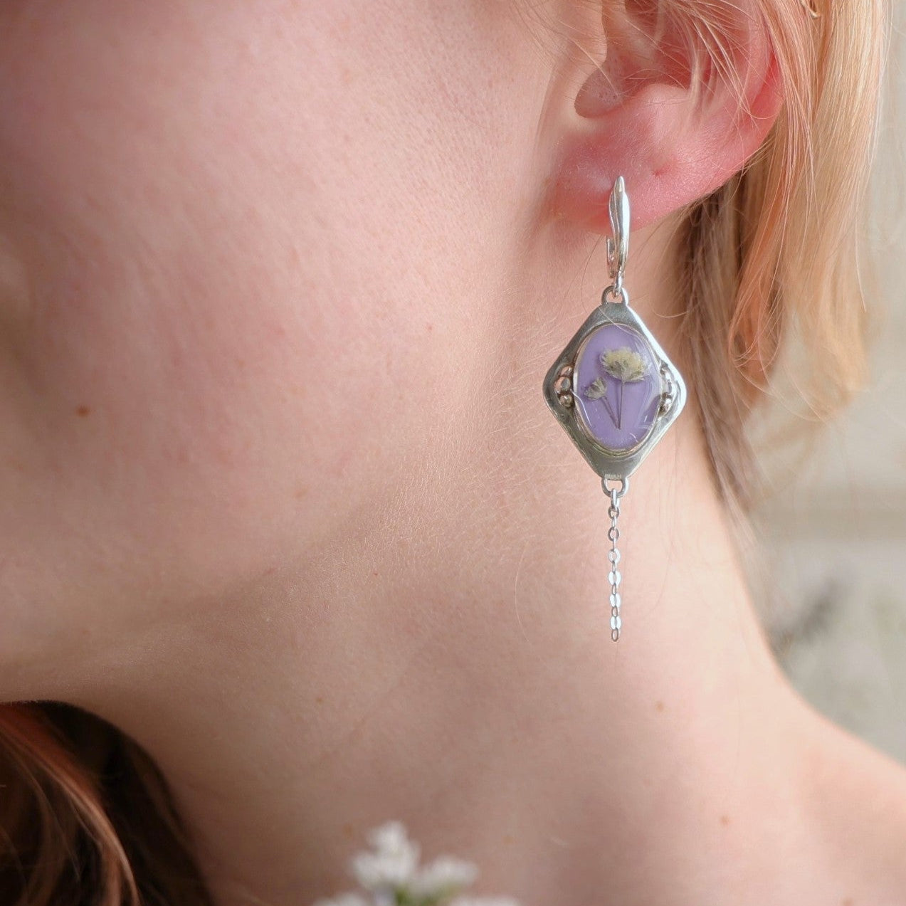 Close-up of a silver earring with a purple stone worn by a person.