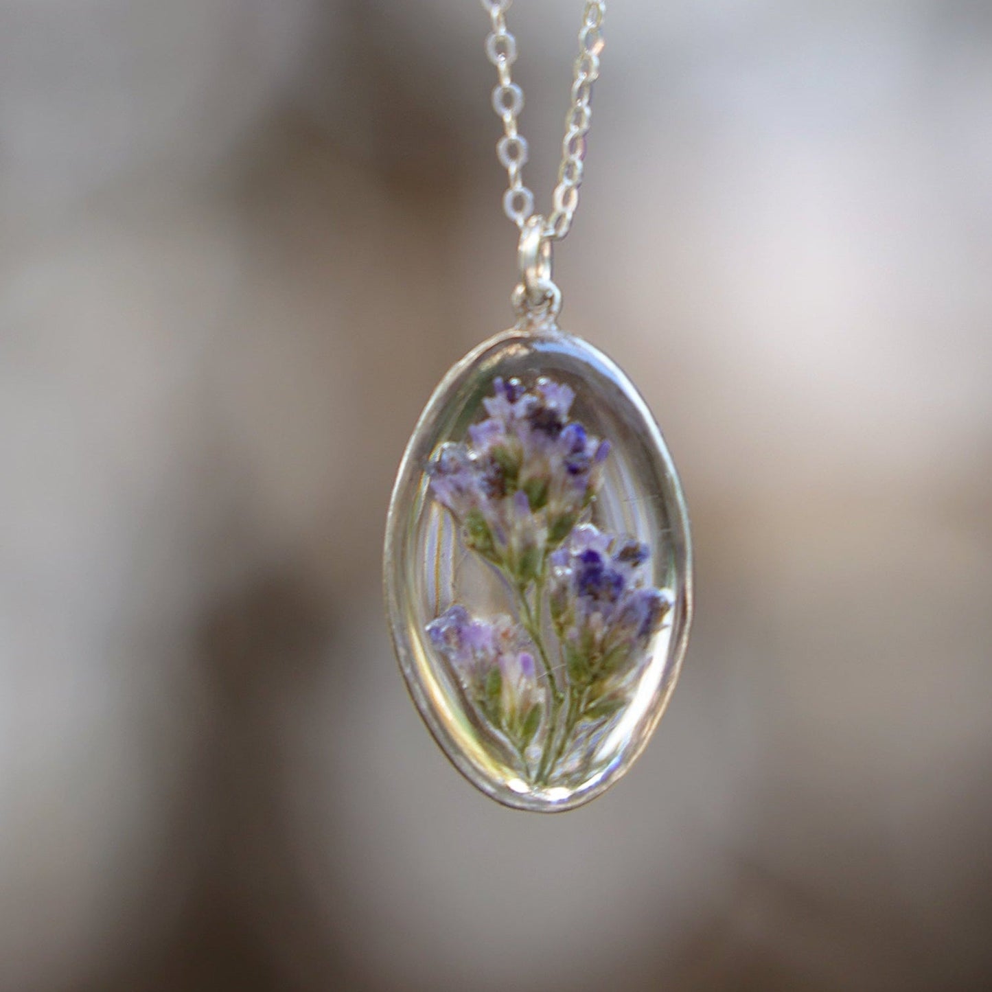 Necklace with a pendant featuring pressed flowers against a blurred natural background