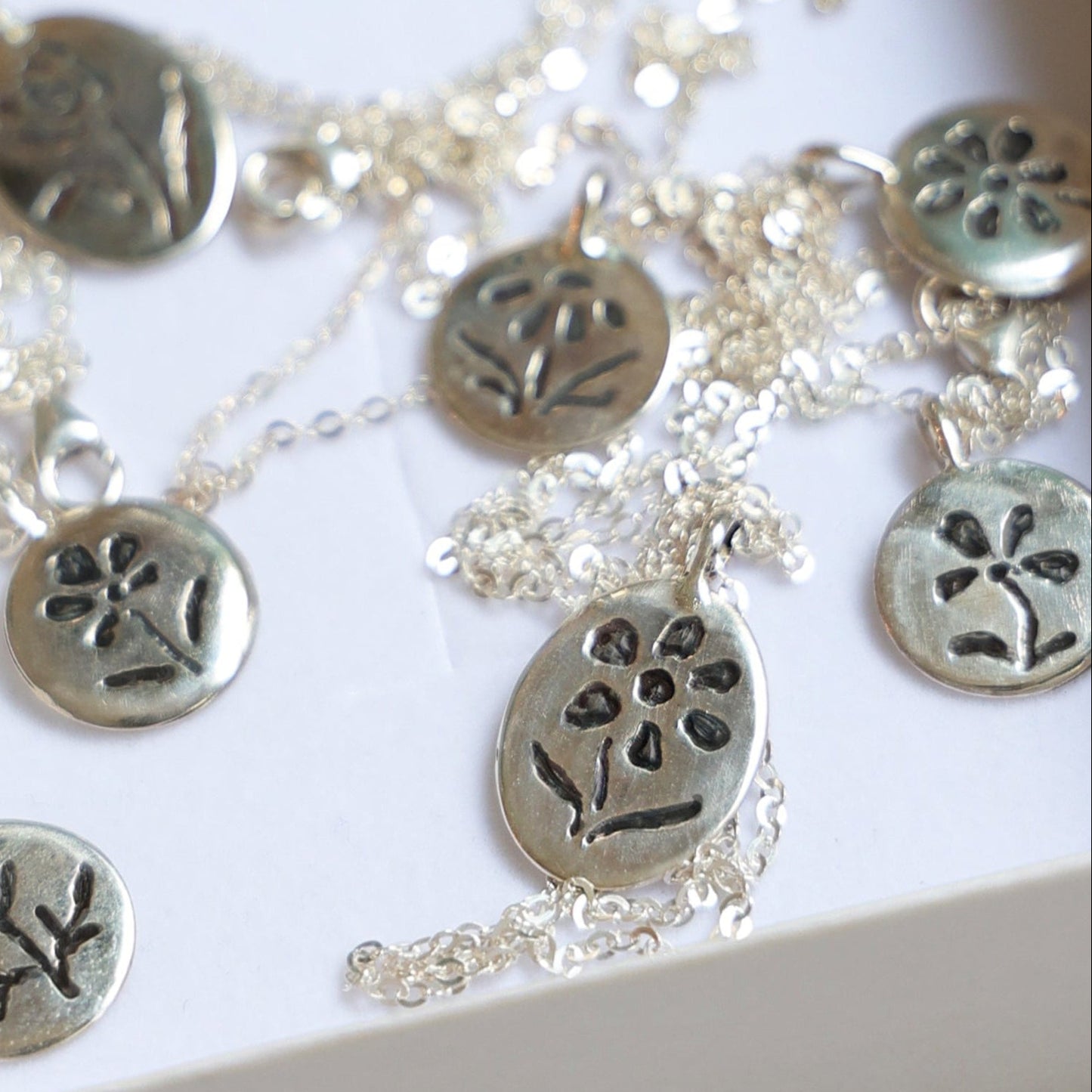 Silver necklace with floral pendants in a white box on a light background
