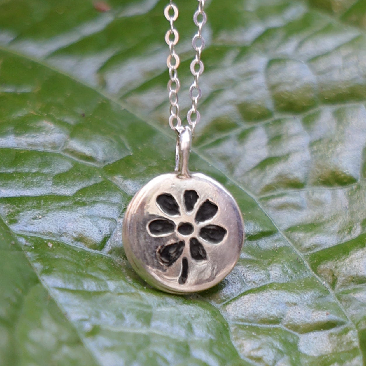 Silver necklace with a floral pendant on a green leaf