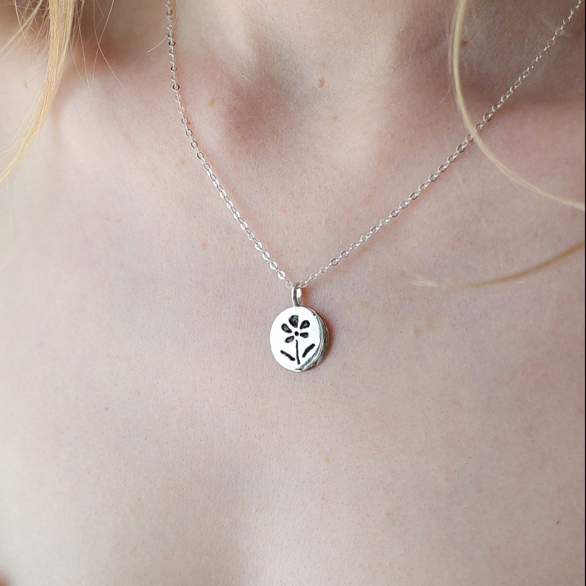 Necklace with a small pendant worn by a person in a white lace top.