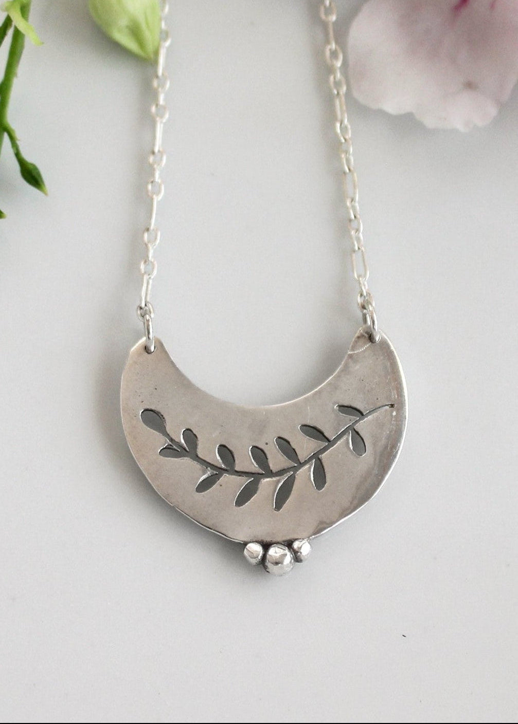 Silver necklace with leaf design on a light background with flowers