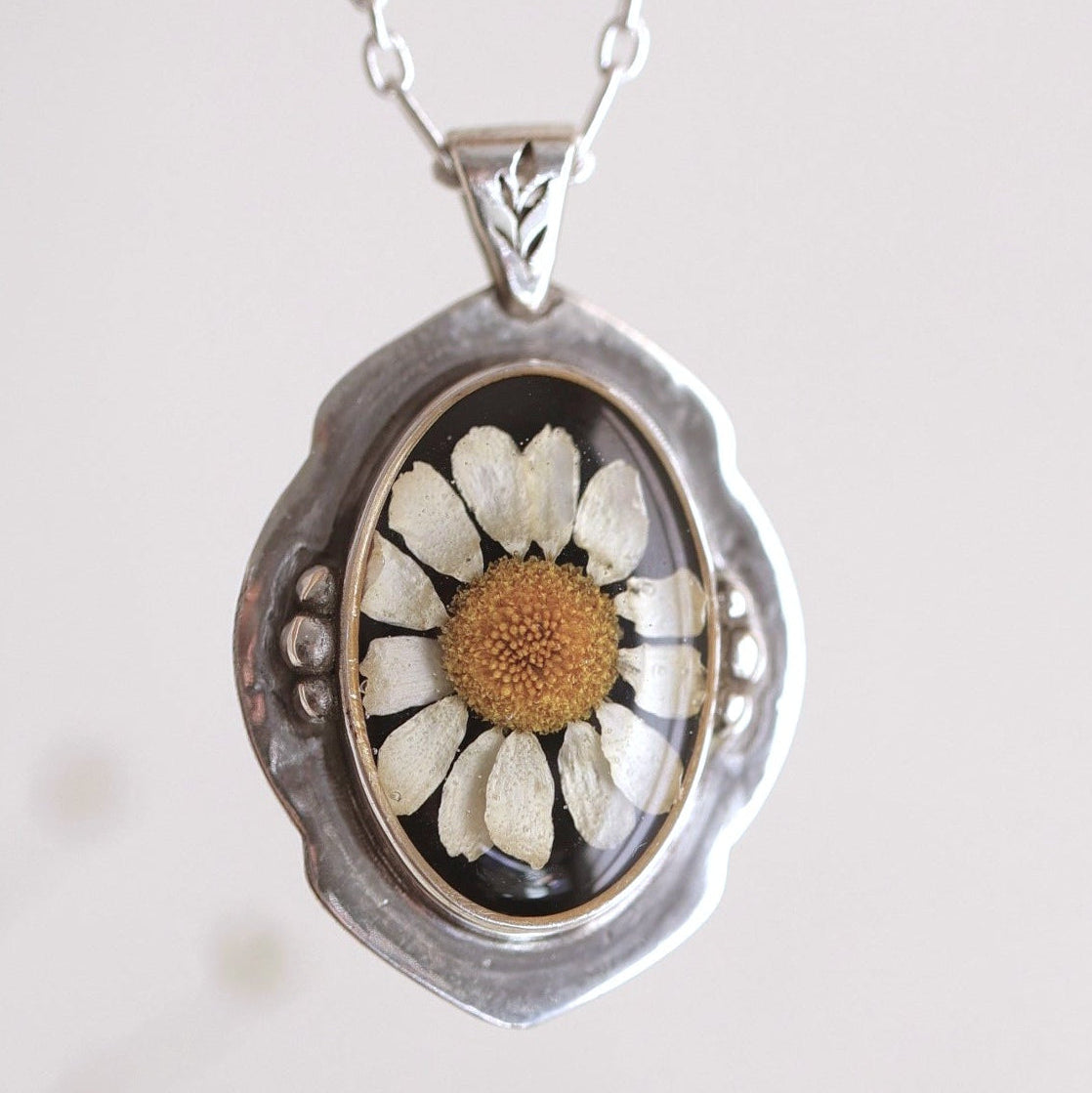 Silver necklace with a pendant featuring a pressed flower on a light background