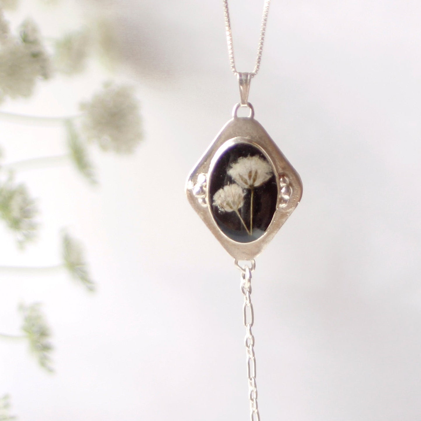 Silver necklace with a pendant featuring dried flowers on a white background