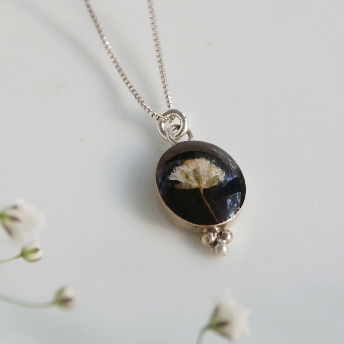 Necklace with a round pendant featuring a black background and white flowers, on a light gray background.