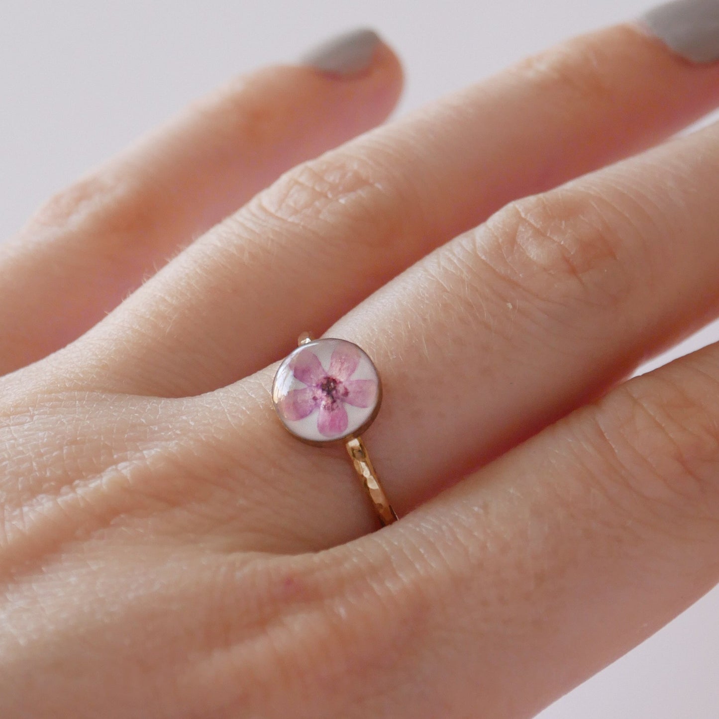 Close-up of a hand wearing a ring with a pink gemstone on a light background