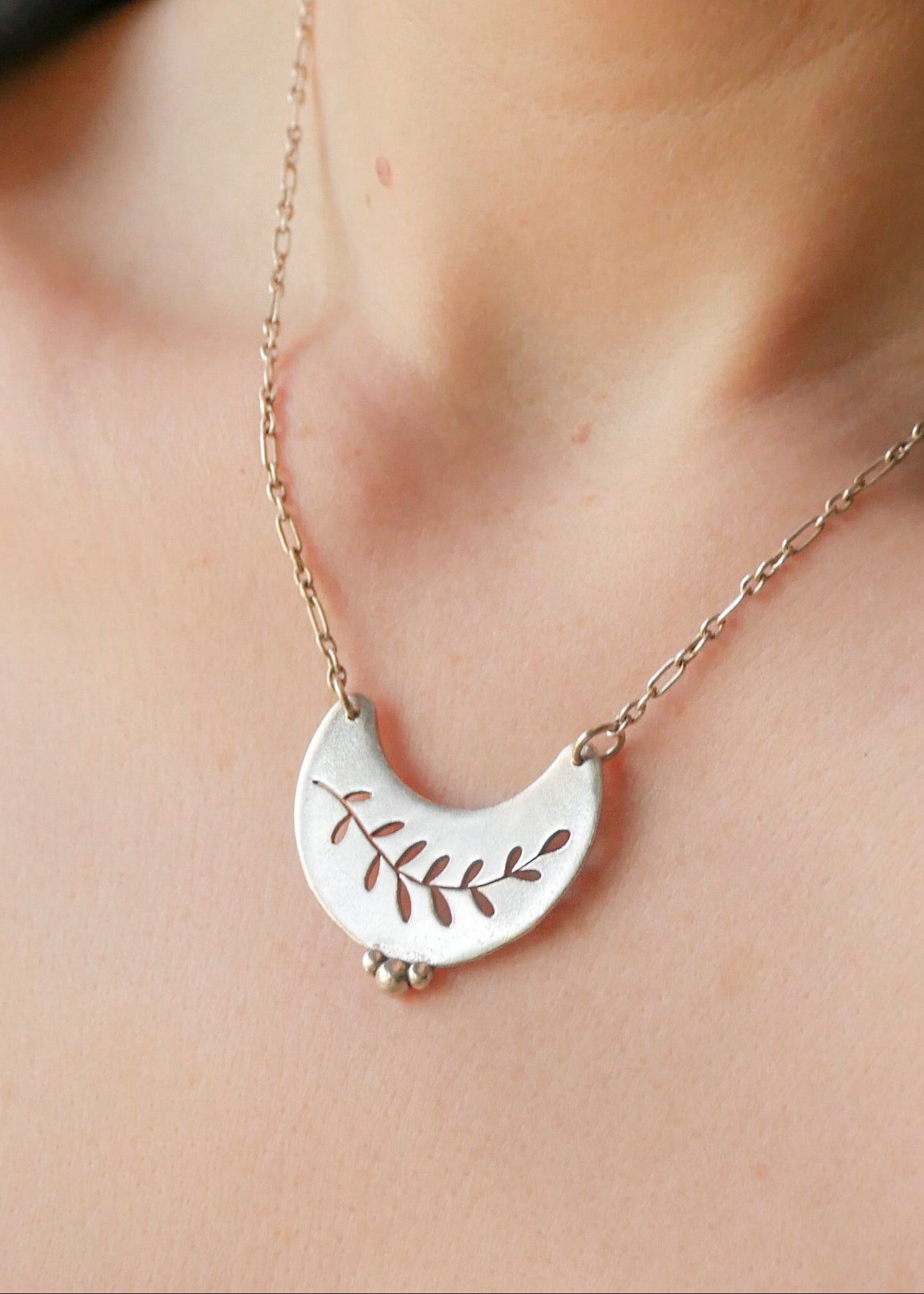 Silver necklace with a leaf design on a person's neck