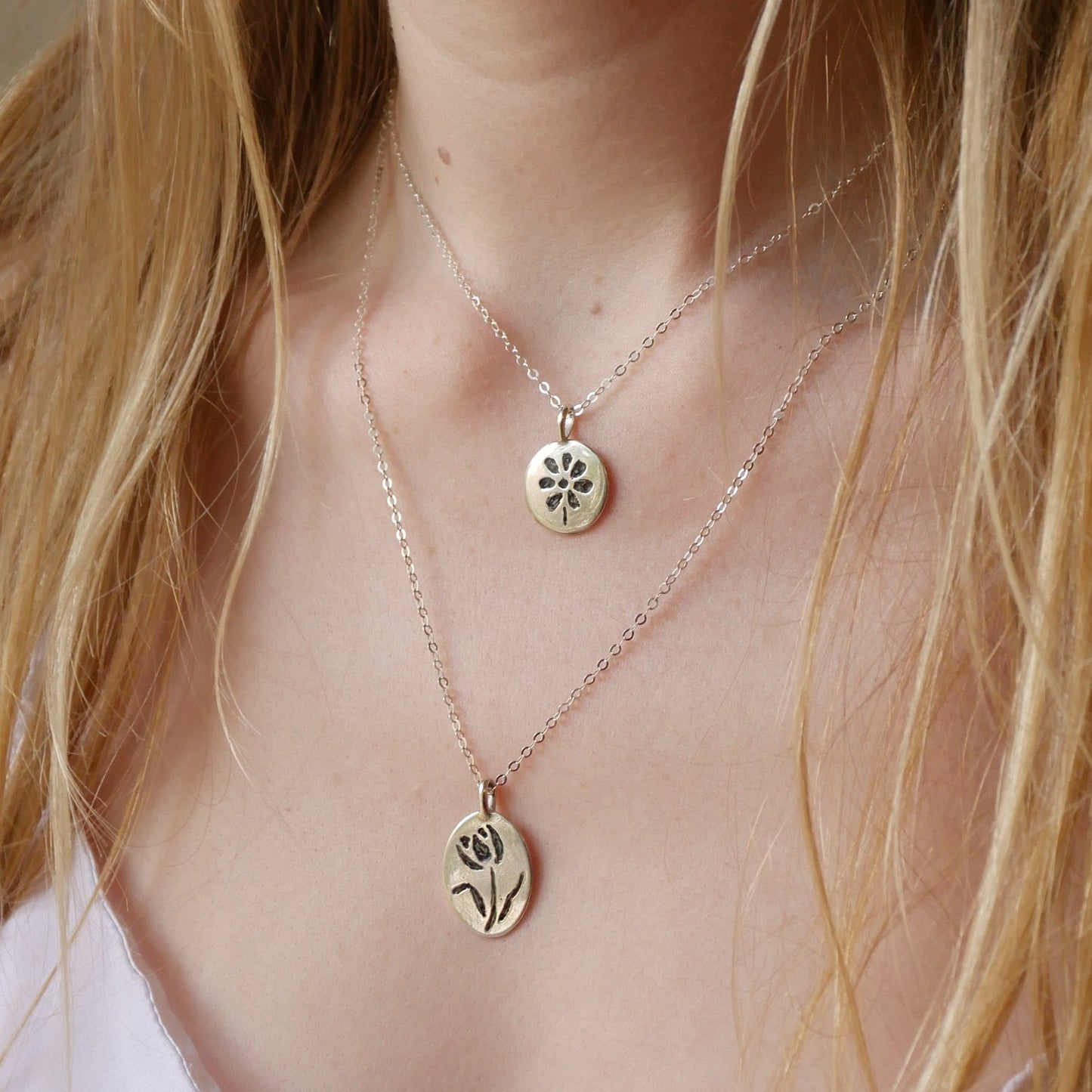 Close-up of a person wearing two delicate necklaces with floral pendants.