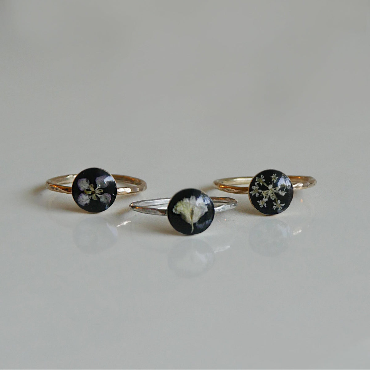 Three floral ring designs on a light gray background