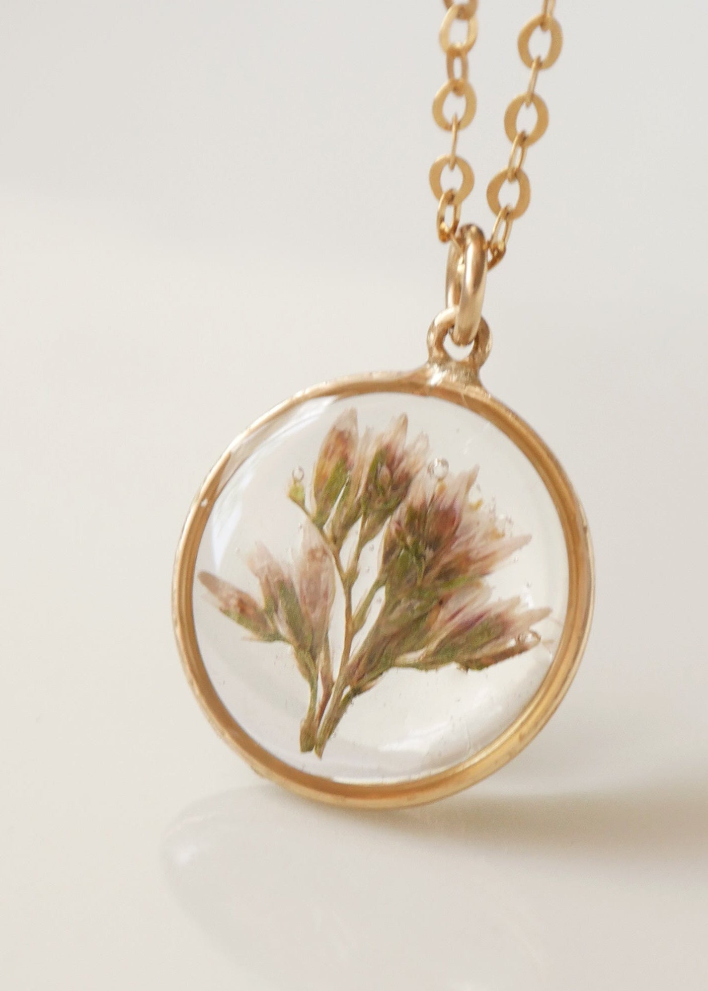 Necklace with a gold chain and round pendant featuring pressed flowers on a light background