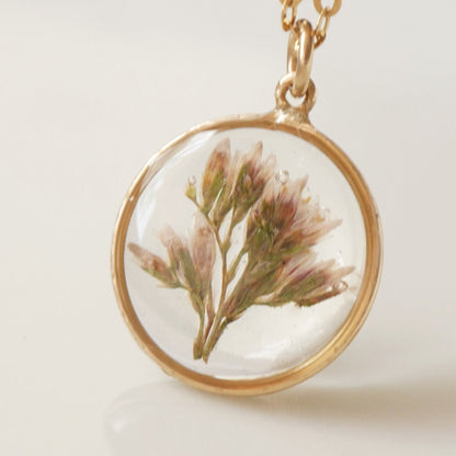 Necklace with a gold chain and round pendant featuring pressed flowers on a light background