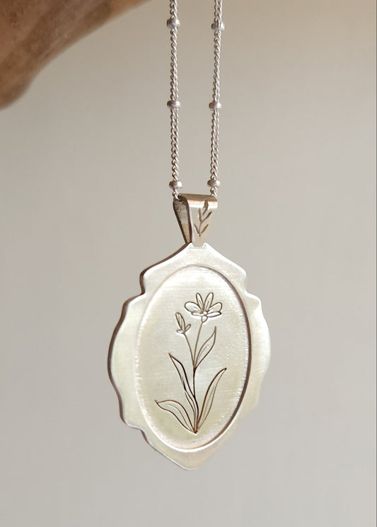Silver locket with floral engraving on a chain against a neutral background