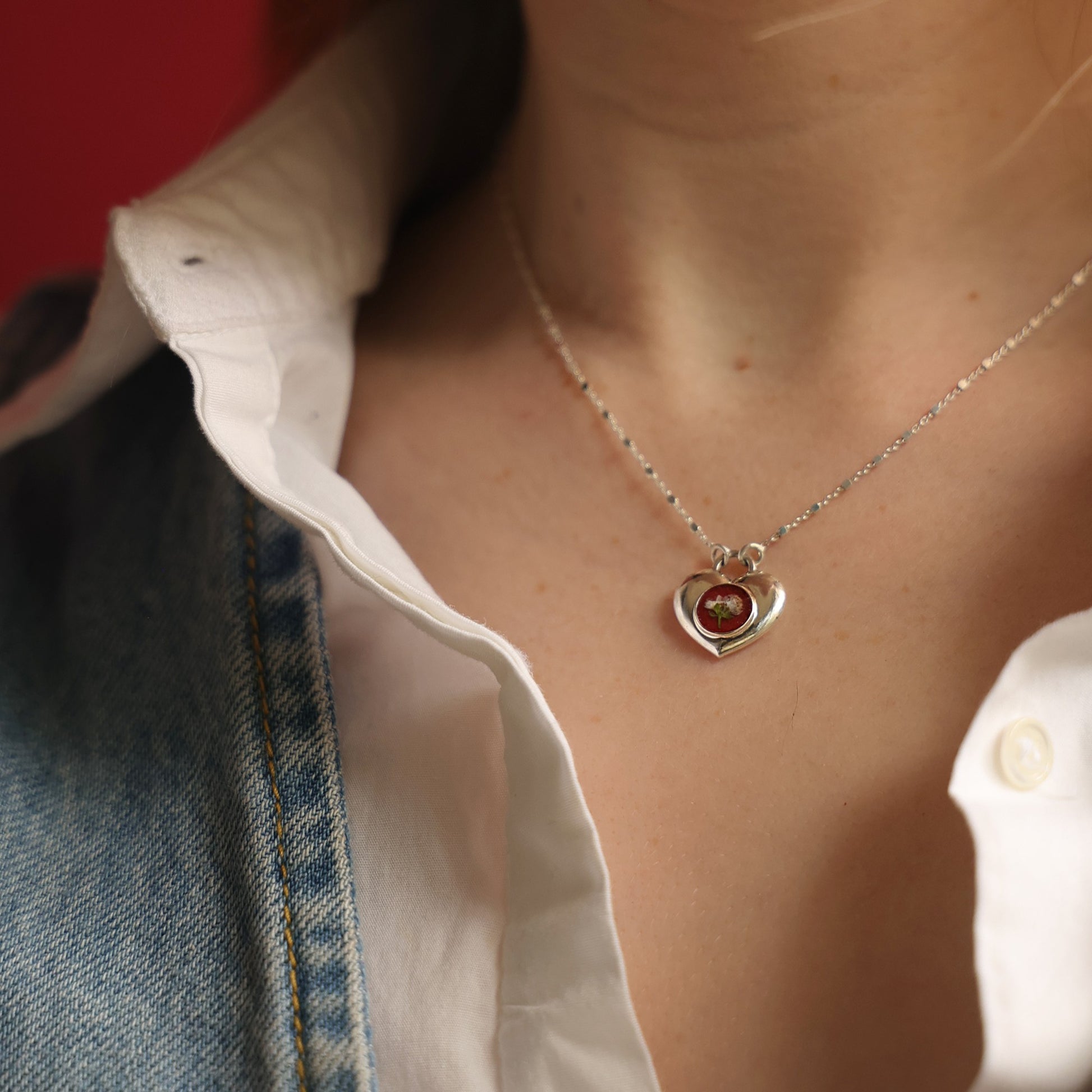 Heart-shaped necklace with a red gemstone worn by a person.