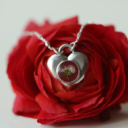 Silver heart-shaped pendant with a red stone on a red rose