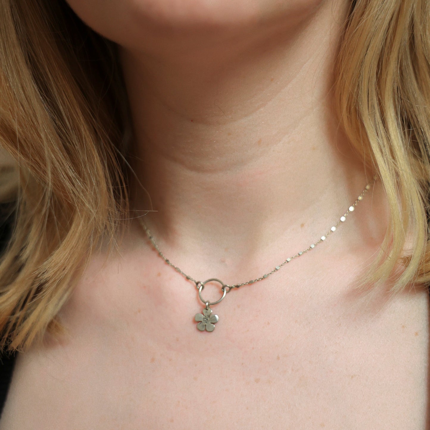 A close-up of a person's neck and chest wearing a delicate silver chain necklace with a small four-leaf clover pendant.