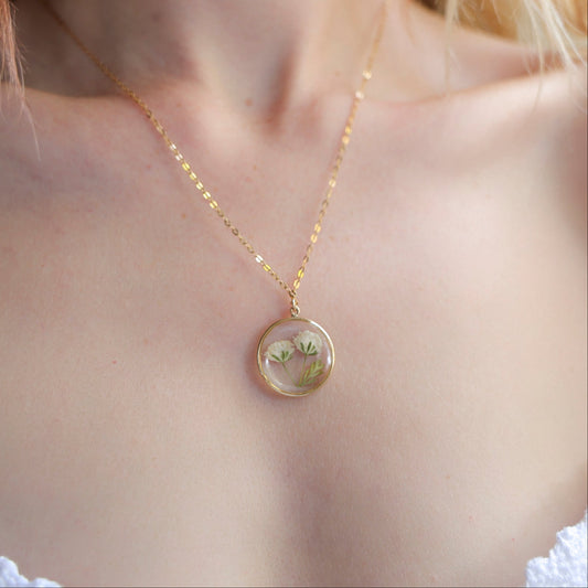 A person wearing a Round Gypsophila necklace with a gold-filled chain and a circular pendant containing preserved Gypsophila flowers.