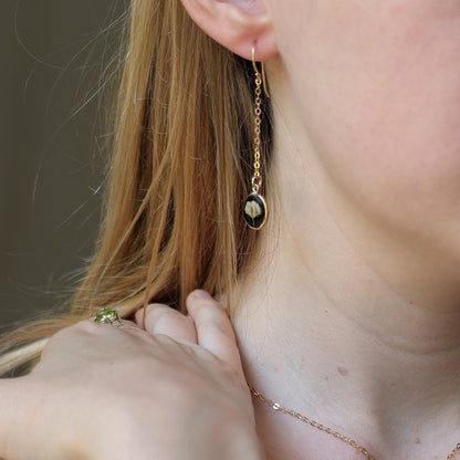 Close-up of a person wearing gold earrings and a necklace with a pendant.