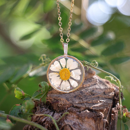 Necklace with a floral pendant hanging on a branch with leaves and blurred background