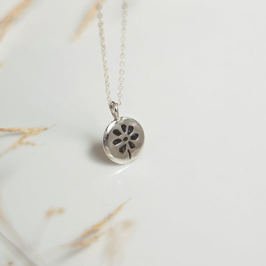 Silver necklace with a floral pendant on a marble surface