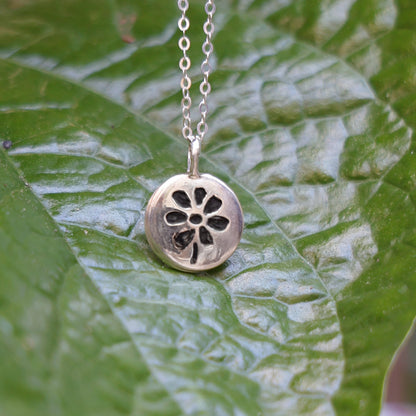Silver necklace with a floral pendant on a green leaf