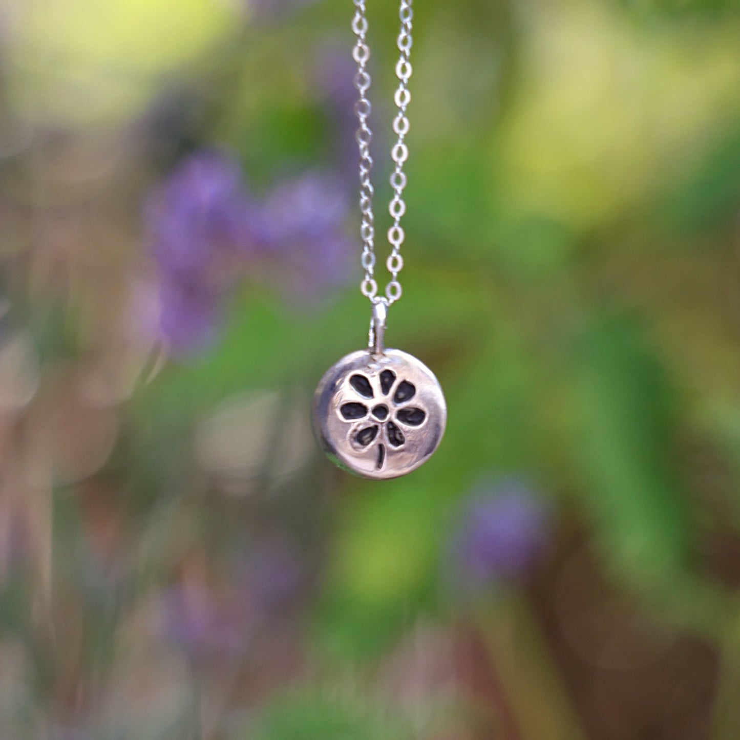 Silver necklace with a floral pendant against a blurred natural background
