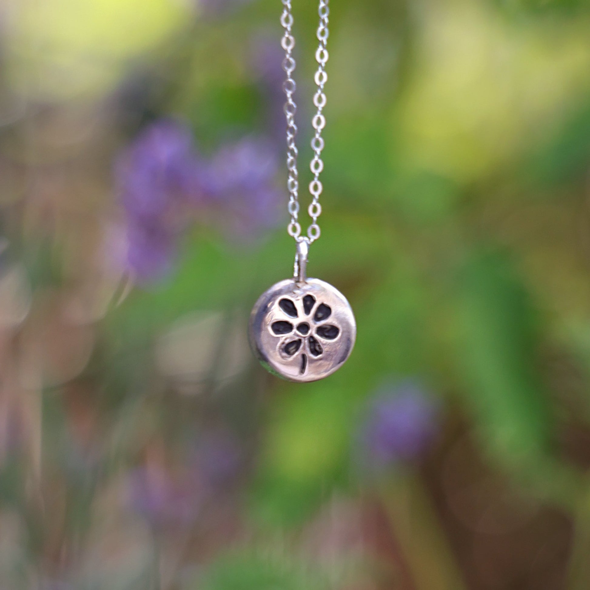 Silver necklace with a floral pendant against a blurred natural background