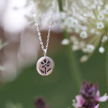 Silver necklace with a floral pendant against a natural background of flowers and plants.