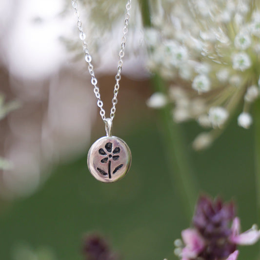 Silver necklace with a floral pendant against a natural background of flowers and plants.