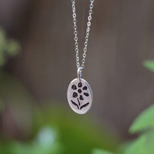 Silver necklace with a floral pendant against a blurred green background