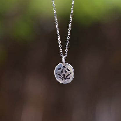 Silver necklace with a floral pendant against a blurred natural background

