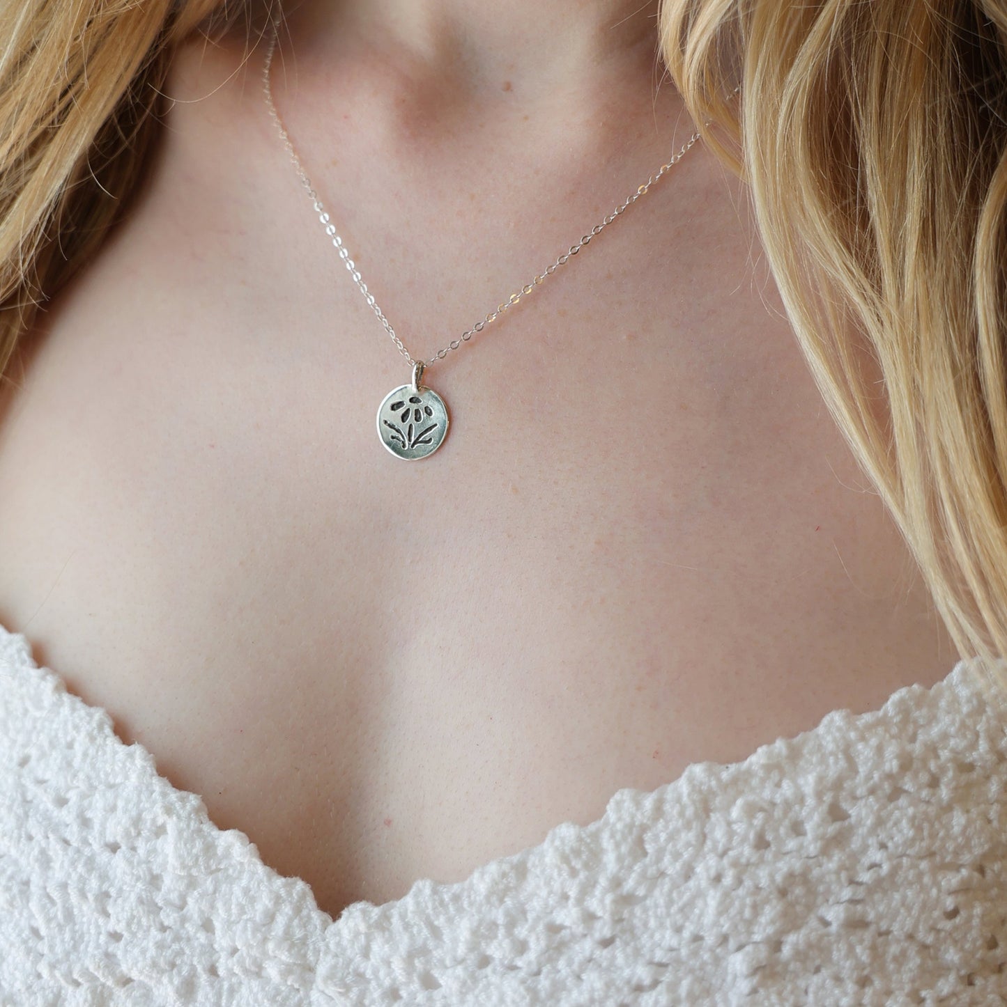 Necklace with a small pendant worn by a person in a white lace garment.
