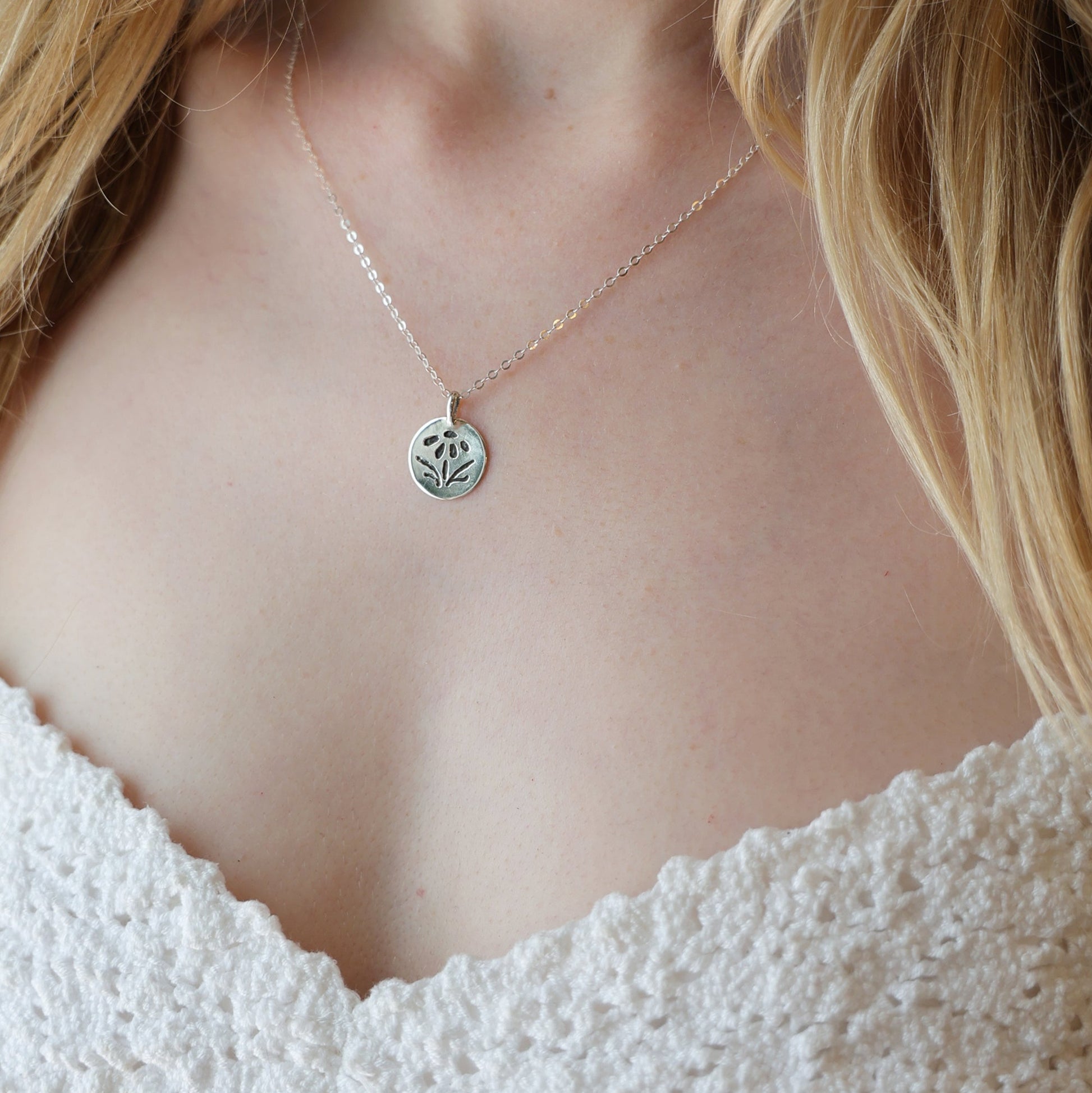 Necklace with a small pendant worn by a person in a white lace garment.