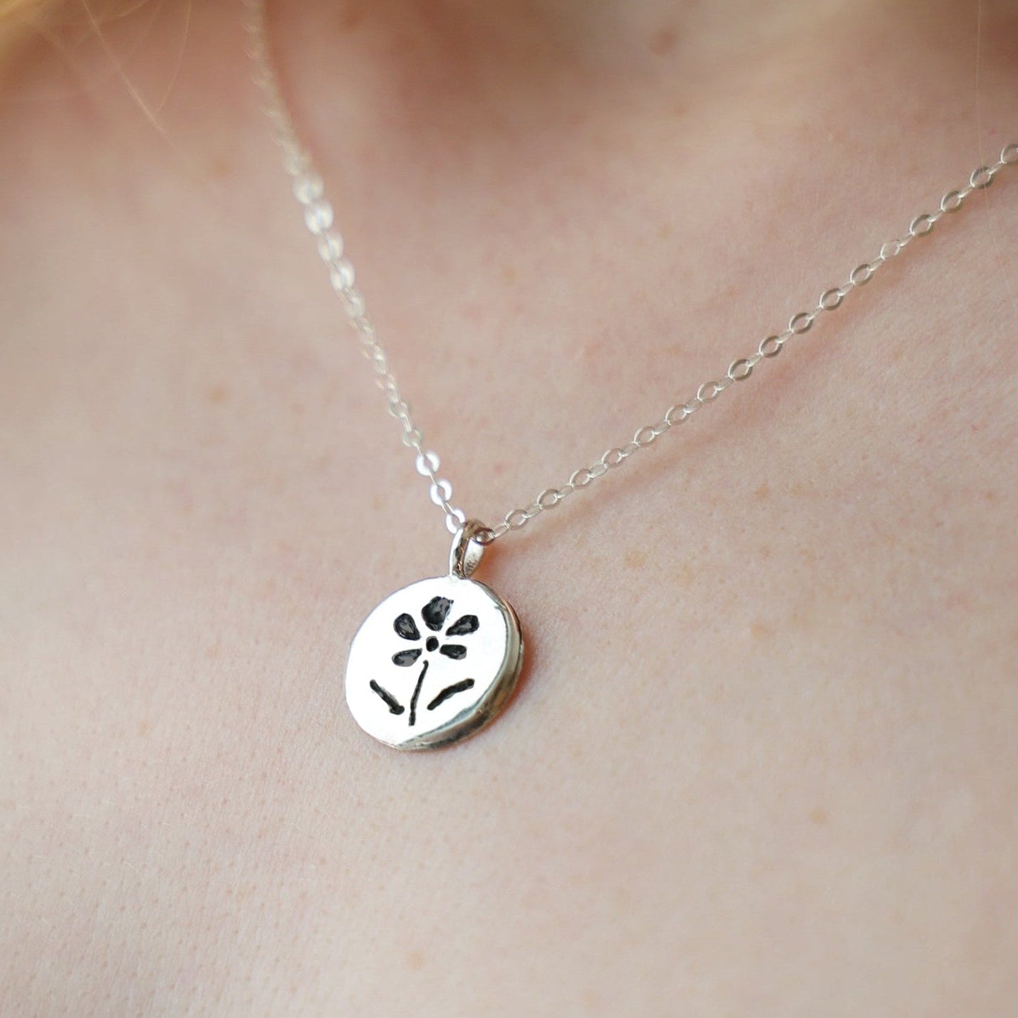 Silver necklace with a floral pendant on a person's neck