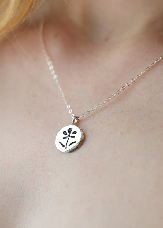 Silver necklace with a floral pendant on a person's neck