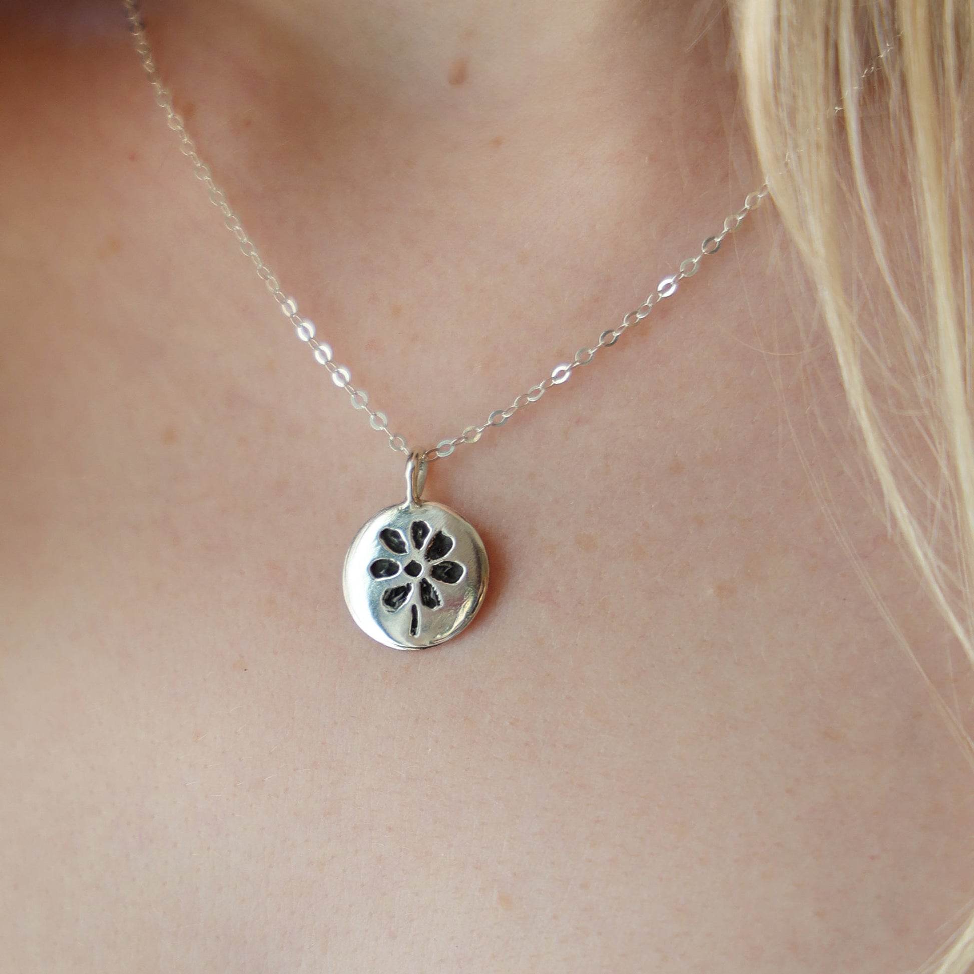 Silver necklace with a floral pendant on a person's neck