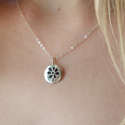 Silver necklace with a floral pendant on a person's neck