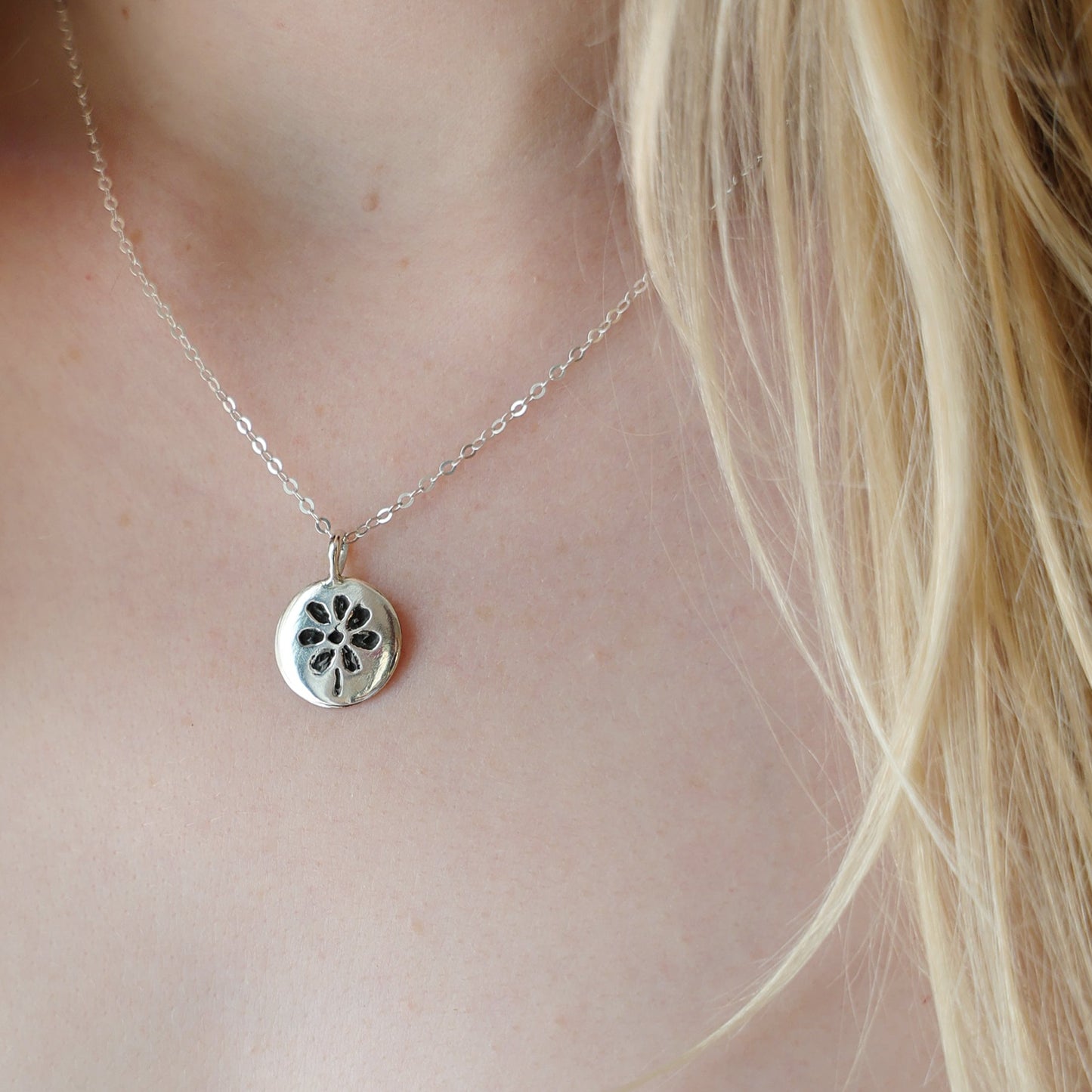 Silver necklace with a pendant worn by a person in a white garment