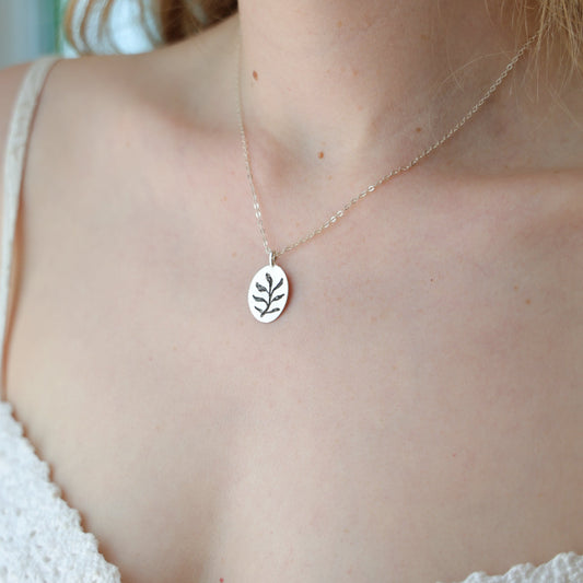 Silver leaf necklace worn by a person in a white textured top.