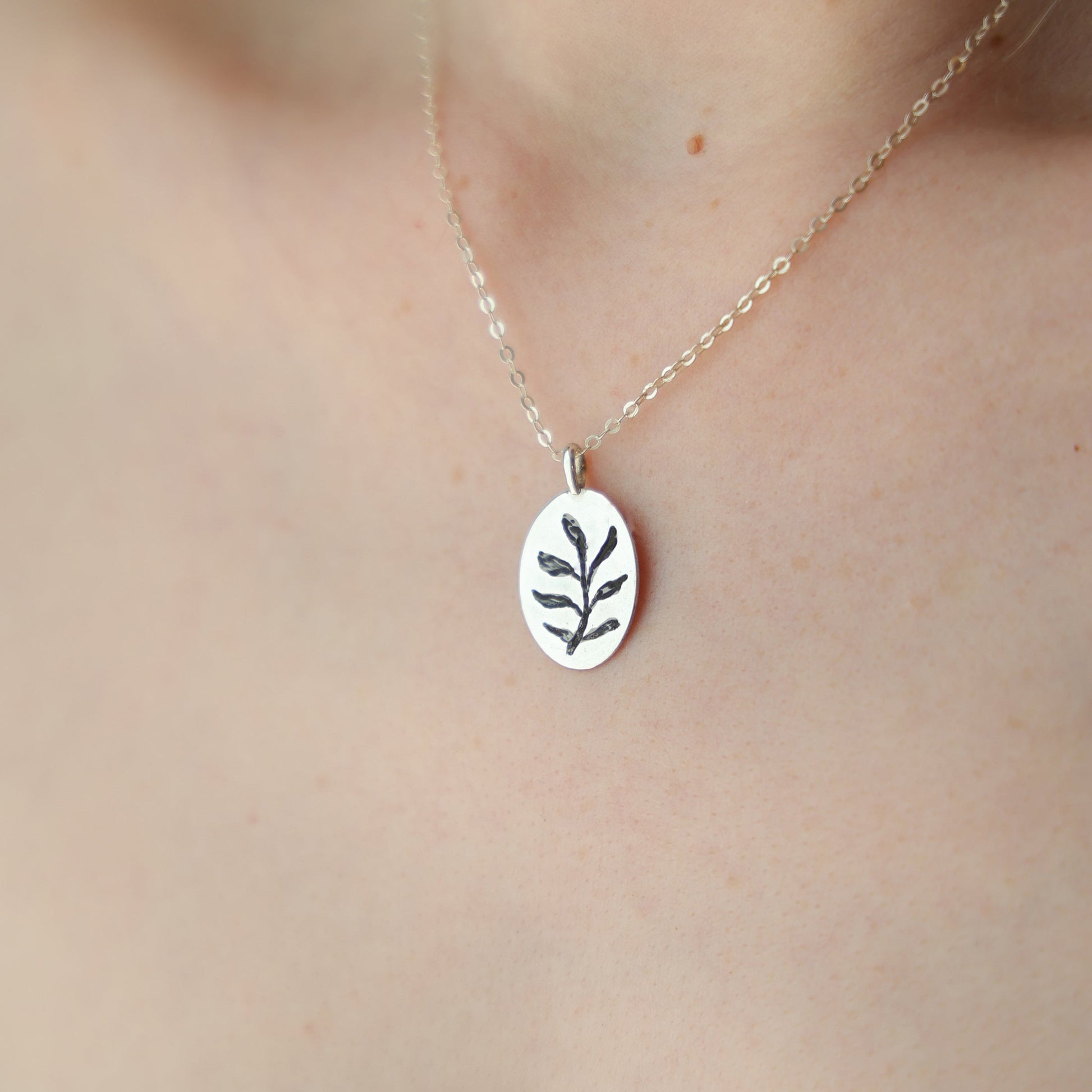 Silver necklace with a leaf pendant on a person wearing a white lace garment.