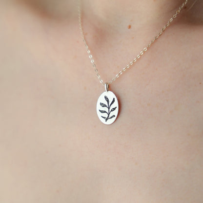 Silver necklace with a leaf pendant on a person wearing a white lace garment.