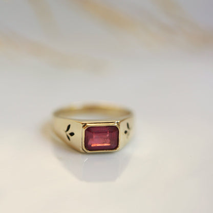 Gold ring with a red gemstone on a light background