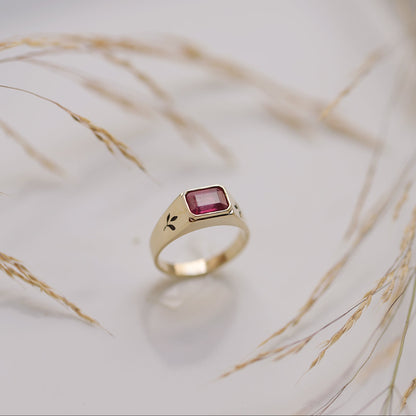 Gold ring with a red gemstone on a light background