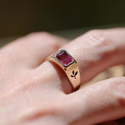 Rose gold ring with a red gemstone on a hand against a blurred background