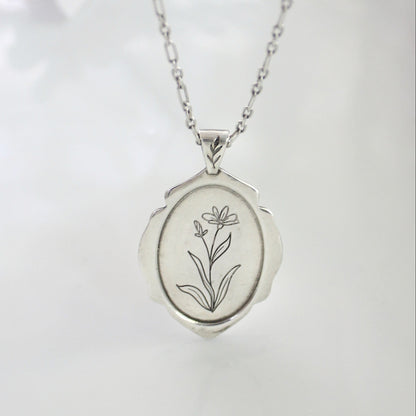 Silver locket with floral engraving on a white background