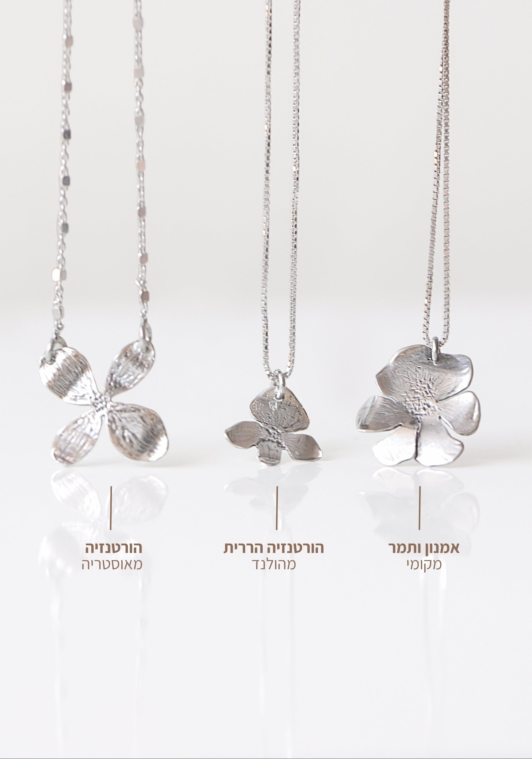 Three silver floral pendant necklaces with textured flower pendants hanging vertically against a clean white background, each with Hebrew text labels below.