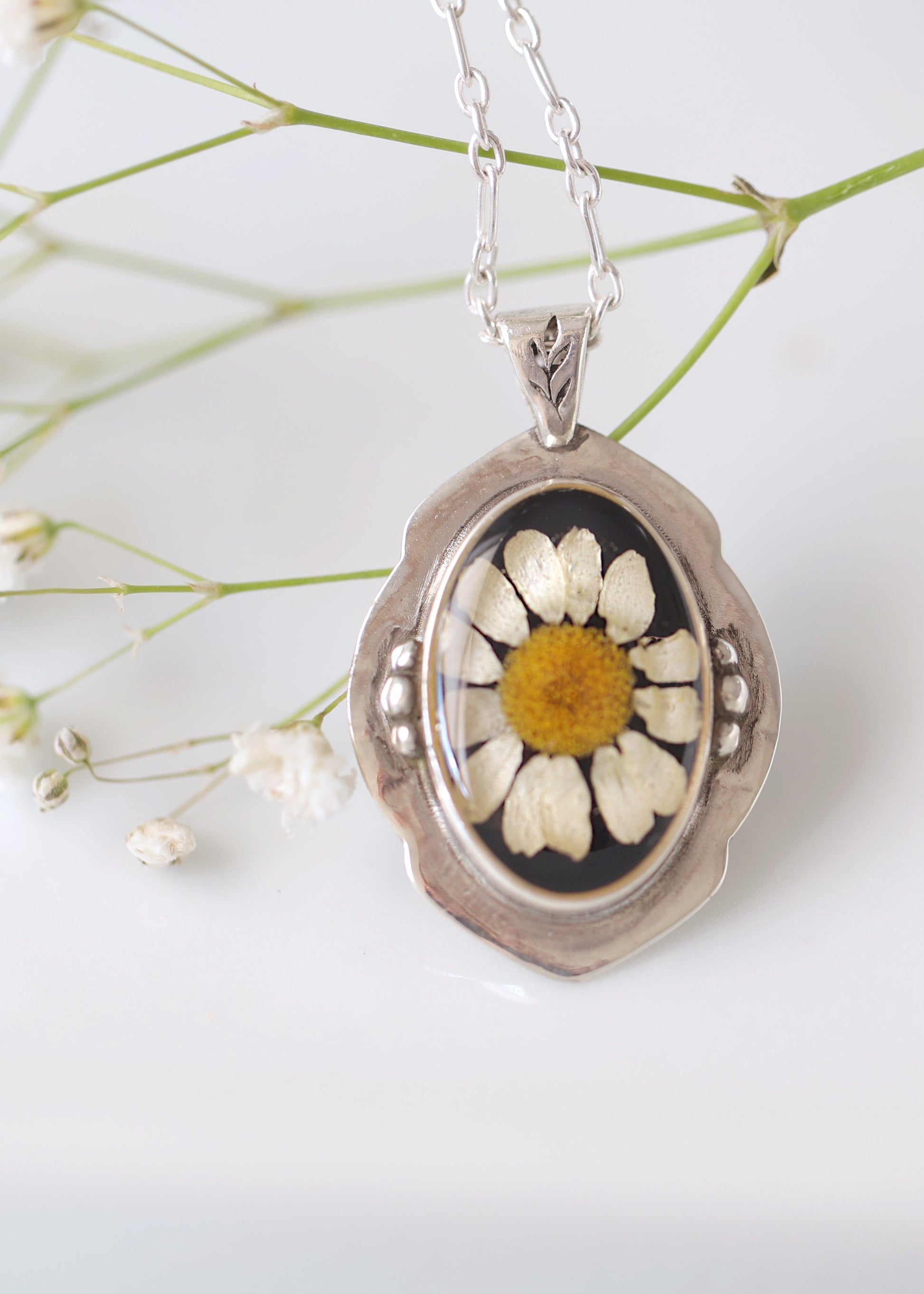 Silver pendant with a pressed flower design on a white background