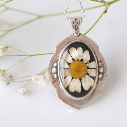 Silver pendant with a pressed flower design on a white background