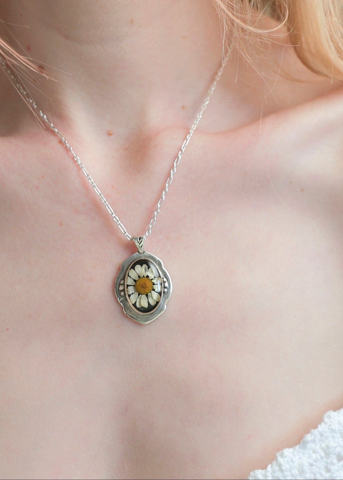 Silver necklace with a locket featuring a flower design on a person's neck.